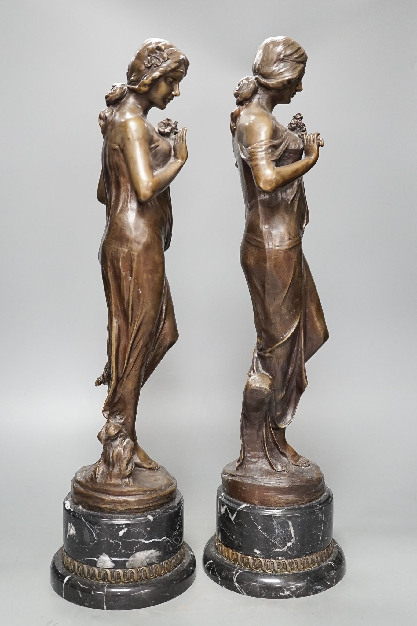 After Jean-Antoine Houdon, (French 1741-1828), a pair of bronze figures of lady’s holding flowers, on marble bases, 52cm